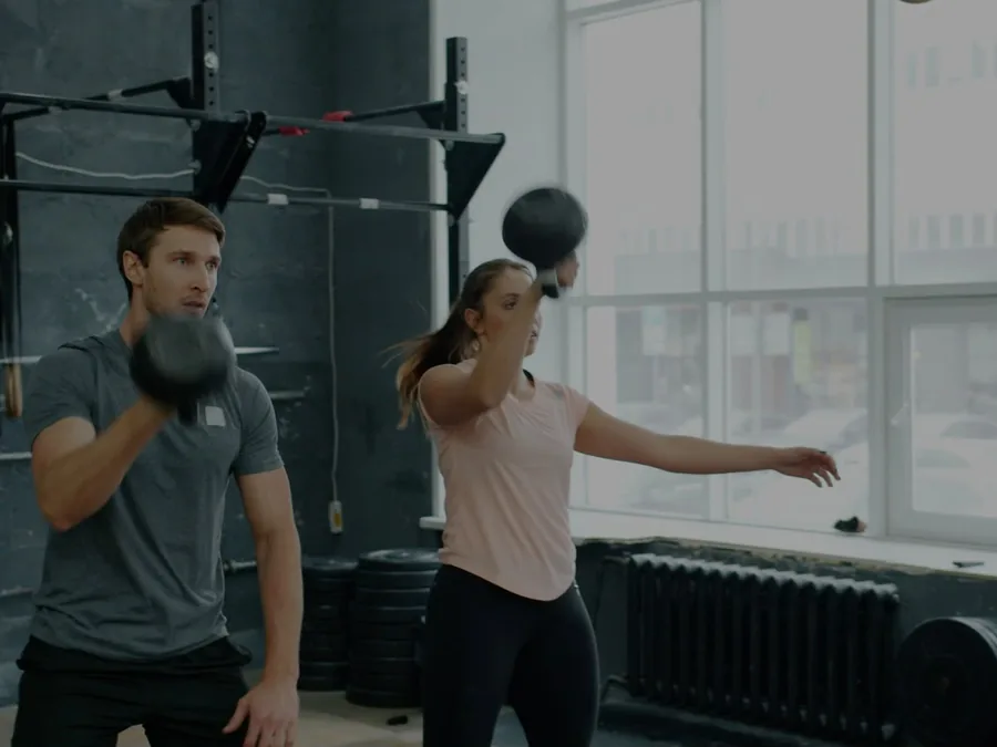 Entrenador y alumna trabajando fuerza con mancuernas en una sesión de entrenamiento personal