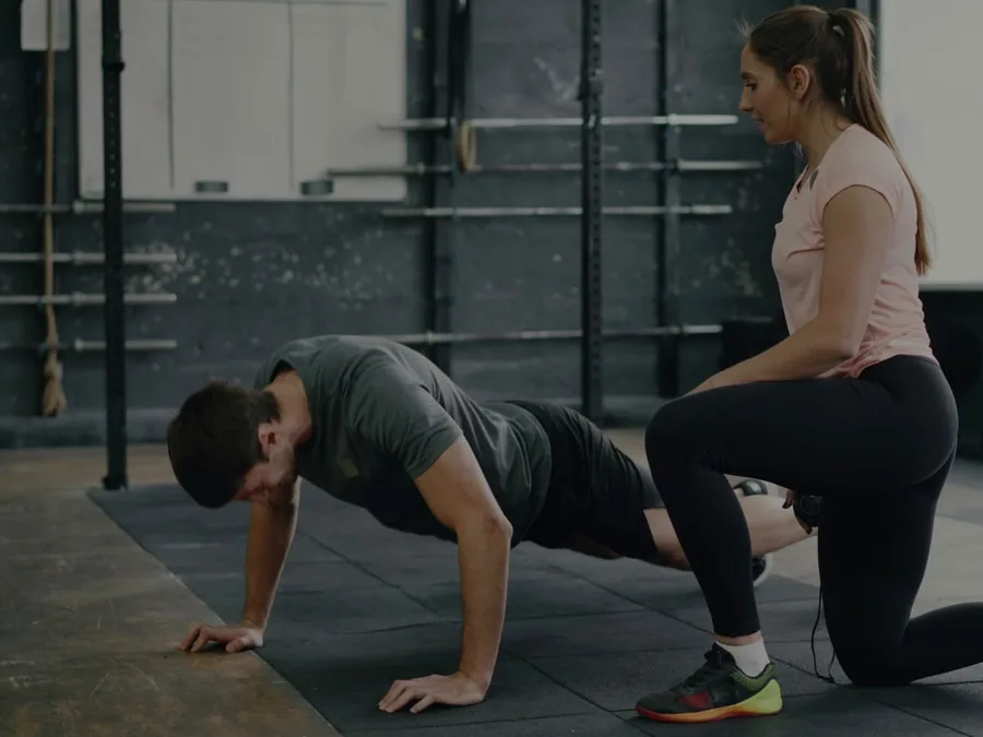 Entrenadora supervisando de cerca a un alumno que hace una flexión durante un entrenamiento en grupo reducido