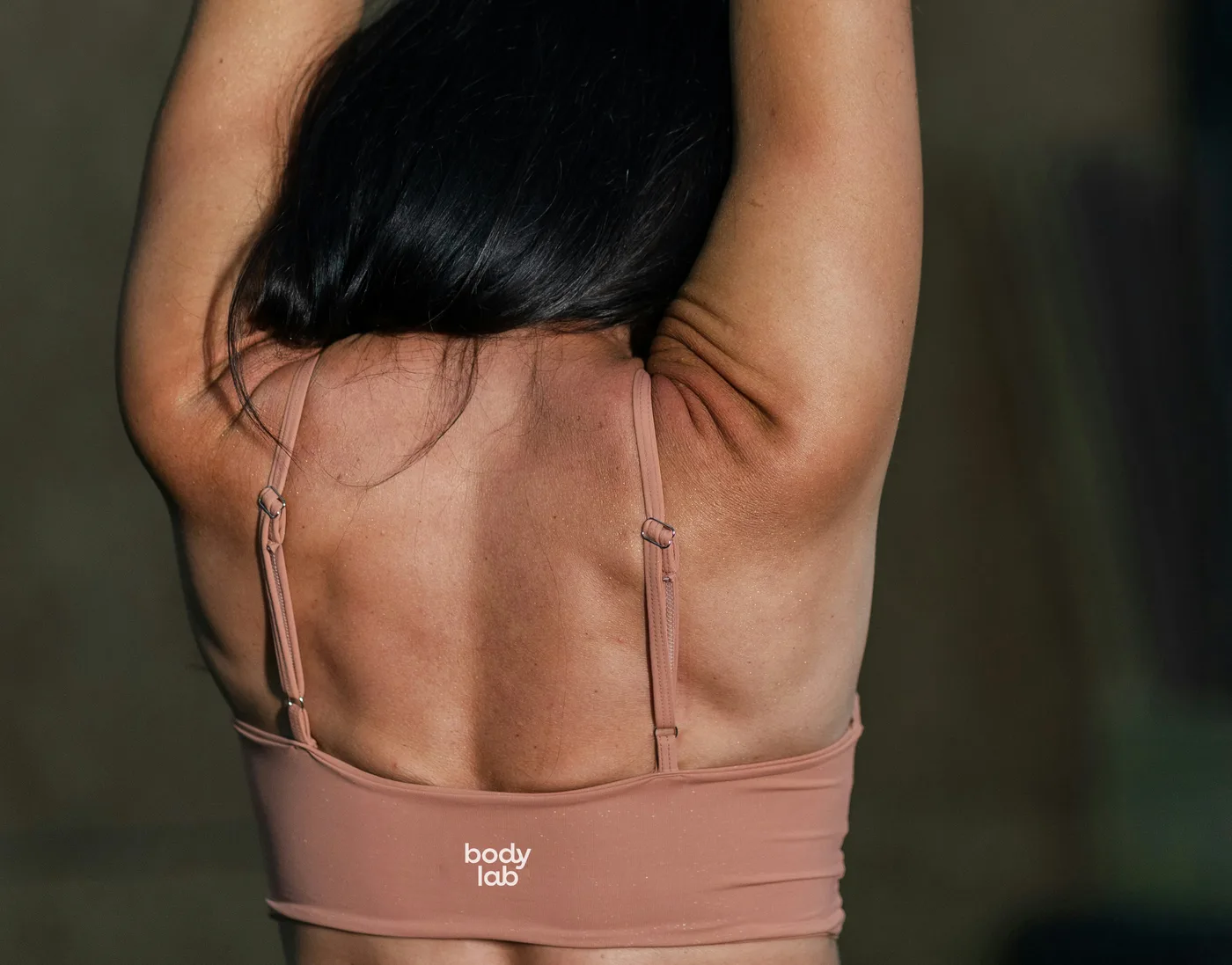 Alumna estirando la espalda con los brazos en alto, con el top de Bodylab